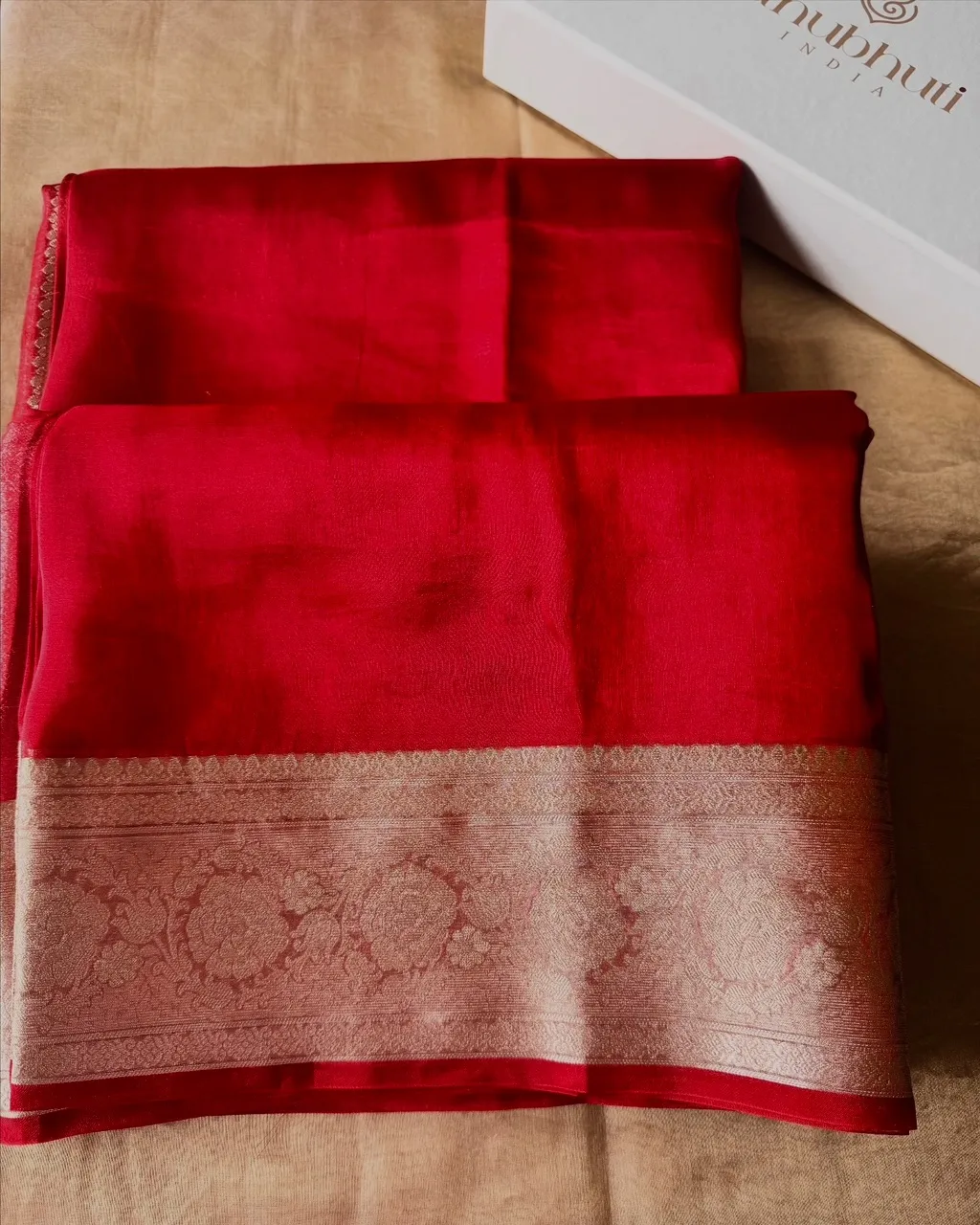 Red brocade tissue silk saree folded beside the white Anubhuti India gift box